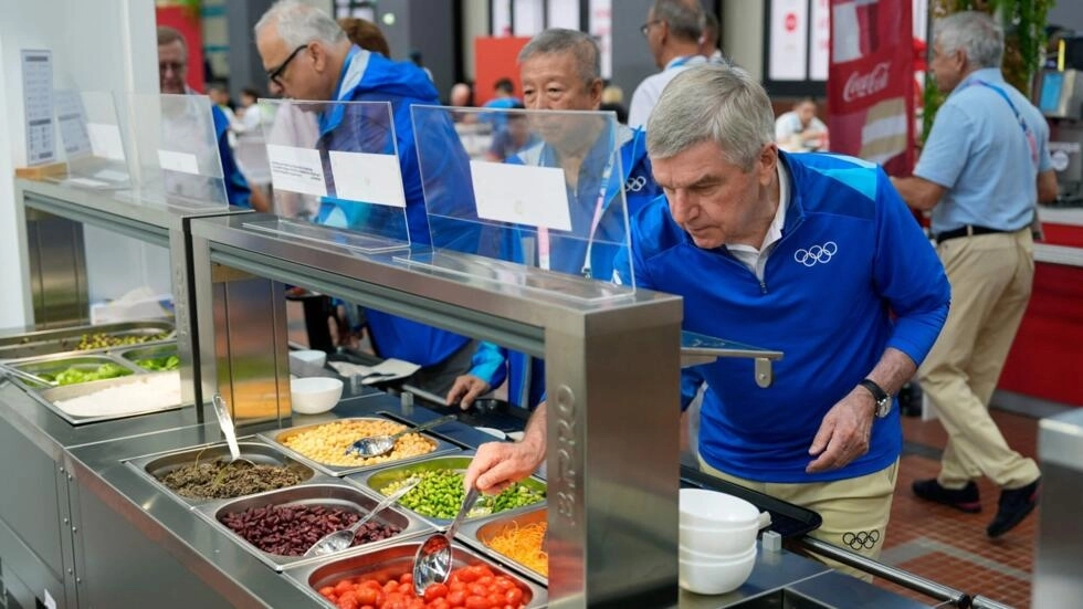 IOCのトーマス・バッハ会長は、2024年7月22日、パリ郊外のサン=ドニのオリンピック村のサラダバーで食べ物を試食します。© デビッド・ゴールドマン / プール / AFP