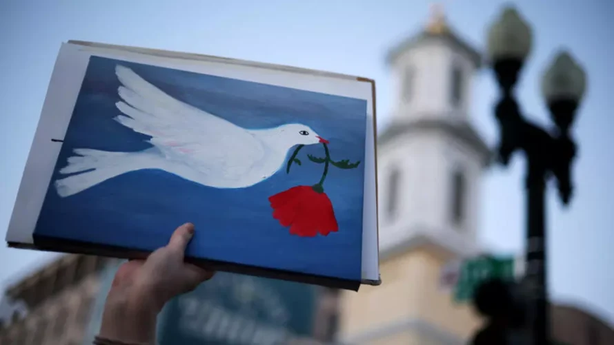 反戦抗議者が、イラン戦争の停戦が宣言された2026年4月7日、ワシントンのホワイトハウス付近での集会において、平和のハトが書かれたプラカードを掲げている。© Getty Images/AFP/Alex Wong