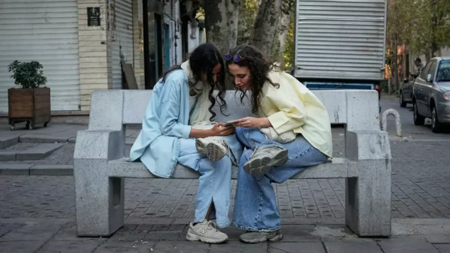 イランのテヘラン北部で、二人の女性がスマートフォンを使用しています。当局は、選択された利用者に対し、より充実したインターネットアクセスを提供するシステムを導入しましたが、多くの人口は依然として厳しい制限が続いています。AP - ヴァヒド・サレミ